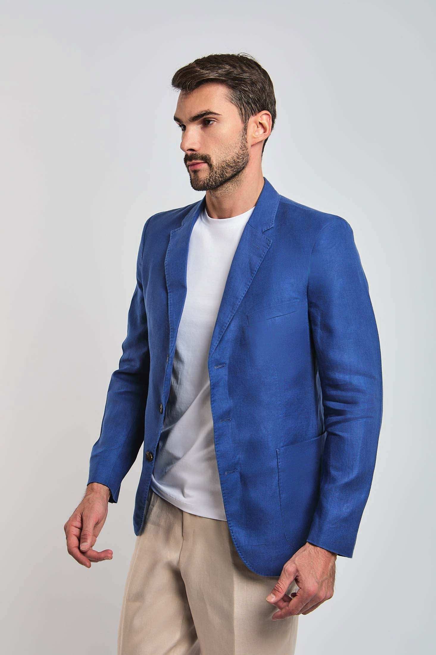 Man wearing a blue blazer, white t-shirt, and beige pants on a plain background