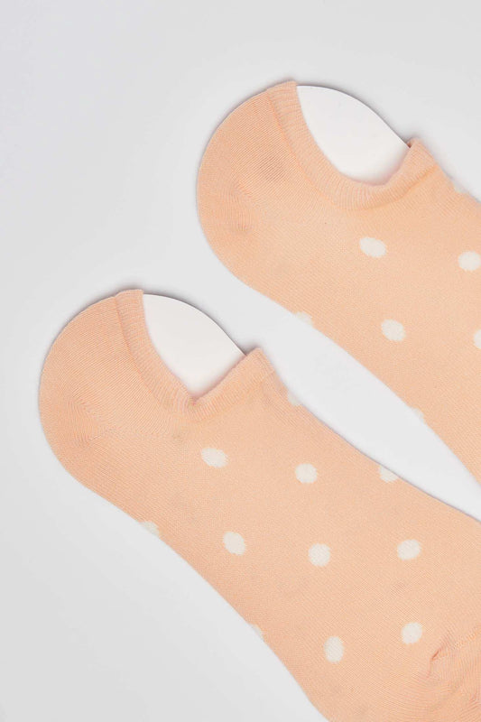 Peach low-cut socks with white polka dots on a plain background